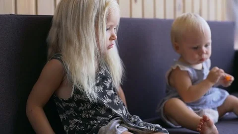 Close up two little blonde sisters sitting on sofa sunny day rapid slow motion Stock Footage 80502458
