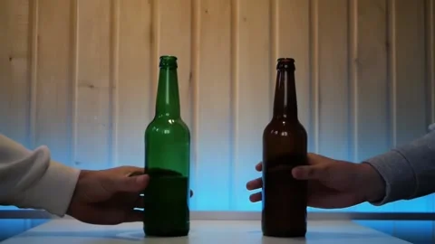 Close up of two male hands clinking a pair of beer bottles in greeting Stockbeeldmateriaal 197079457