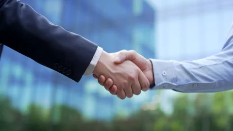 Close up of two male professionals shaking hands outdoors with a blurred office  Stock Footage 332472072