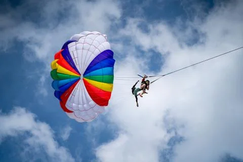 Close up of two men parasailing from below with a rainbow parachute 写真素材