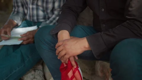 Close-up of two men sitting outdoors reviewing paperwork, one holding a red Stock Footage 327462492