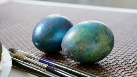 Close-up of two painted Easter eggs and three paintbrushes on a table. 4K Stock Footage 122940588