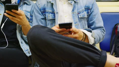 Close up of two people in denim jackets sitting in a subway car with smartphones Stock Footage 151971164