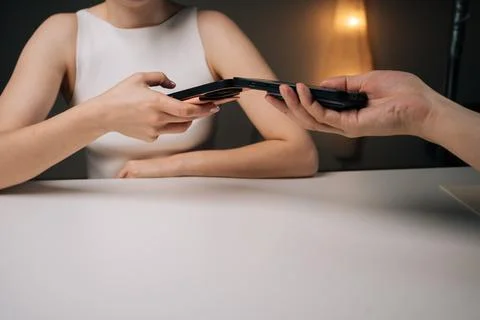 Close-up two people exchanging data using mobile phones sitting at white table Stock Photos