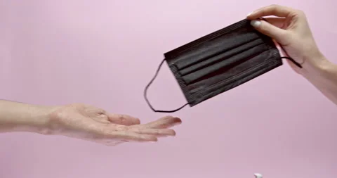 Close up of two people hands sharing with black medical mask over pink Stock Footage 146393383