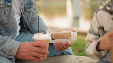 Close up of two people holding coffee and sandwich at wooden table outdoors Stock Footage 346722147