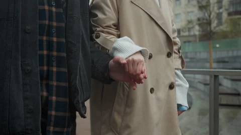 Close up of two people holding hands in outdoor urban setting with trench coat Stock Footage 344879248