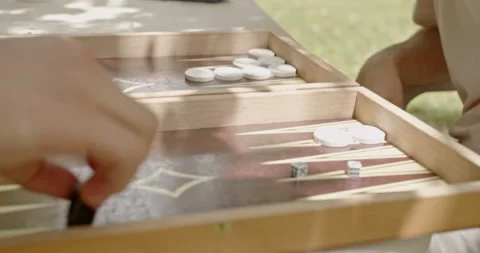 Close-up of two people playing backgammon outdoors, enjoying a sunny day. Dice Stock Footage 281965020