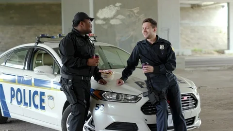 Close up two policemen drinking coffee and eating donut with appetite talk near Stock Footage 112956233