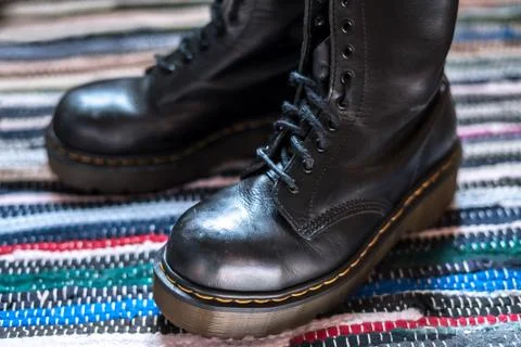 Close-up of two robust, black ankle leather boots on a colorful rug Stock Photos