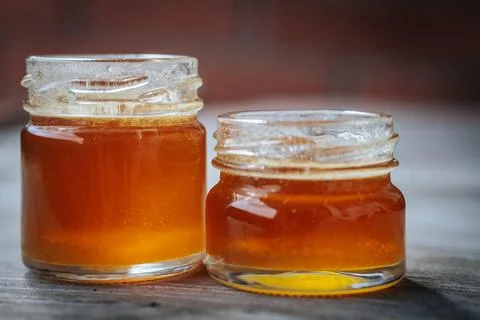 Close-up of two small glass jars filled with golden amber honey placed. Stock Photos