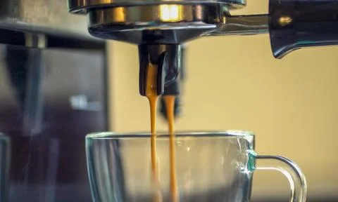 Close up two streams of foaming espresso coffee are poured into a glass Stock Photos