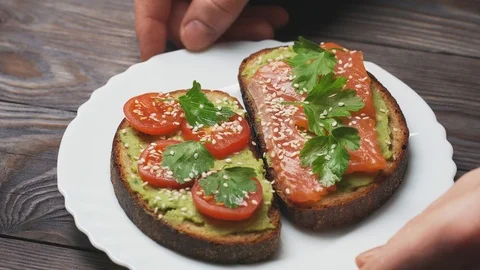 Close-up of two toasts with avocado, salmon fillet and cherry tomatoes on a Vidéo 104769183