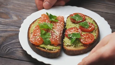 Close-up of two toasts with avocado, salmon fillet and cherry tomatoes on a Stock Footage 104769193