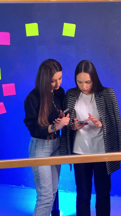 Close-up of two women checking smartphone by board Vertical video. Stock Footage 342934734
