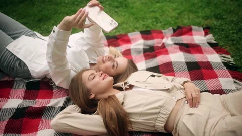 Close up of two women laying down on green grass in a park and taking a selfie Stock Footage 197008124