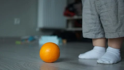 Close-up, a two-year-old baby raises an orange from the floor. Children and Stock Footage 122010380