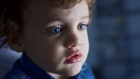 Close up of a two years old kid wearing a denim shirt watching TV in a dark room Stock Footage 98435982