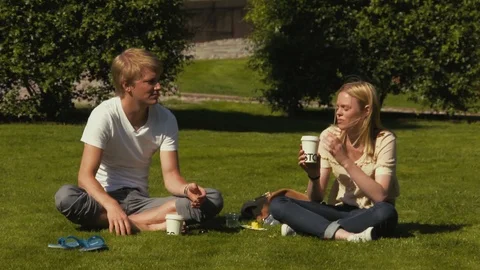 Close up of two young blonde students sitting on grass drinking coffee and Stock Footage 102814650