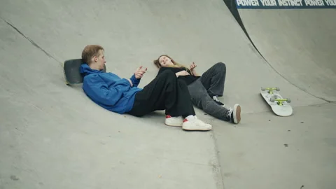 Close up of two young skaters lying in a concrete skatepark, smiling and talking Video stock 340538567