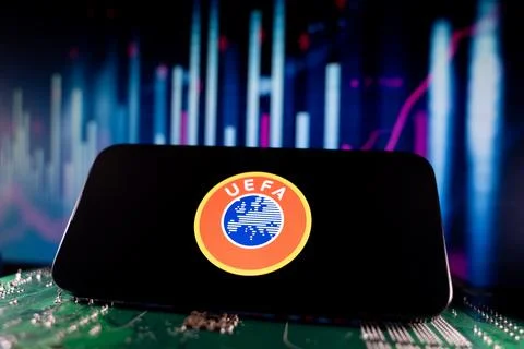 Close up of UEFA logo on smartphone screen with financial chart background. Stock Photos