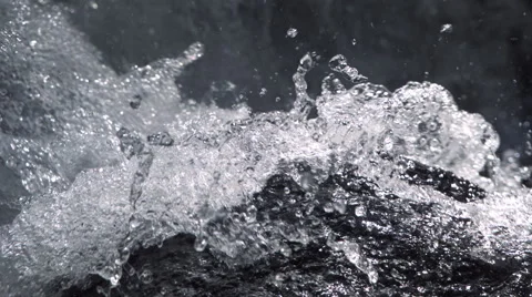 Close-up ultra-slow motion water breaking against a black rock in foreground Stock Footage 59527795