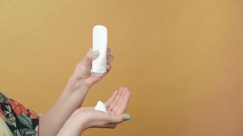 Close-up of unknown woman's hand squeezing white cream in her hand on yellow Stock Footage 154126707