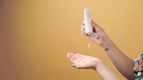 Close-up of unknown woman's hand squeezing white cream in her hand on yellow Stock Footage 154126722