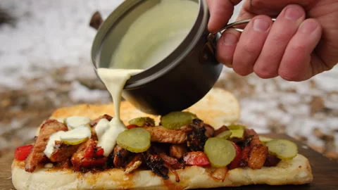 Close up of unknown young man pours cheese sauce on sandwich near campfire Stock Footage 308717785