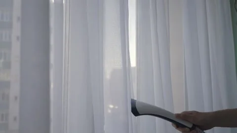 Close-up of unrecognizable housekeeper steaming white curtains in hotel room Stock Footage 304860885