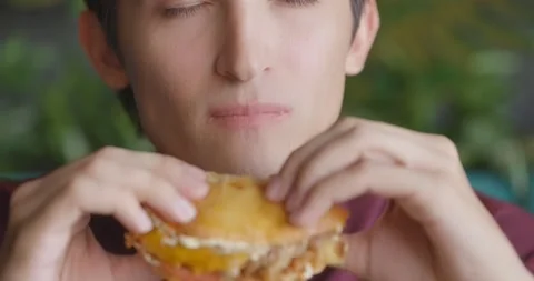 Close up of unrecognizable man eating a burger in a cafe. Front view. Slow Stock Footage 163998043