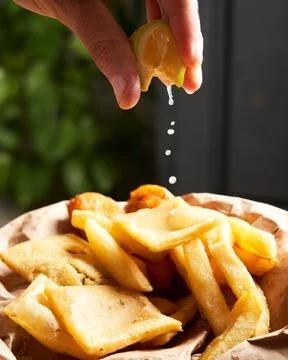 Close-up of unrecognizable man squeezing a lemon smoothly over french fries. Stock Photos