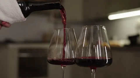 Close-up of unrecognizable person pouring red wine from bottle into two elegant Stock Footage 313222033