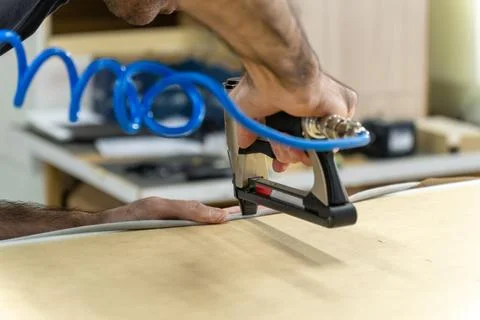 Close-up of upholsterer using a pneumatic staple gun to attach fabric to a .. Fotos de archivo
