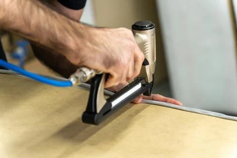 Close-up of upholsterer using a pneumatic staple gun to attach fabric to a .. 写真素材