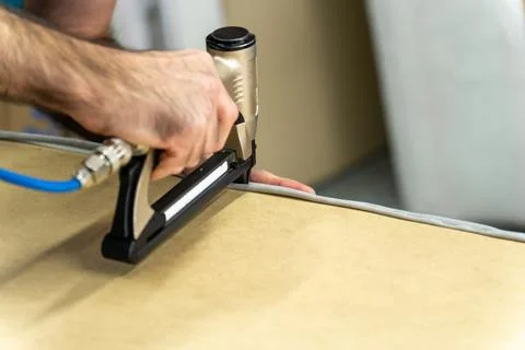 Close-up of upholsterer using a pneumatic staple gun to attach fabric to a .. Stock Photos