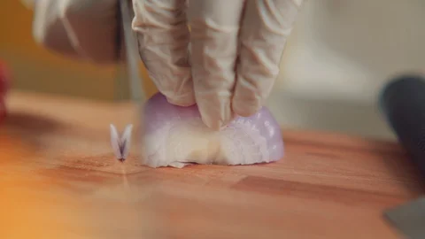 Close-ups chef in gloves is cutting half an onion with sharp knife on wooden Stock Footage 105285187