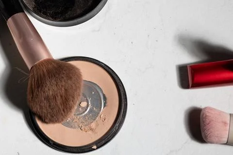 Close-up of a used powder compact and worn brushes on marble, showing residue Stock Photos