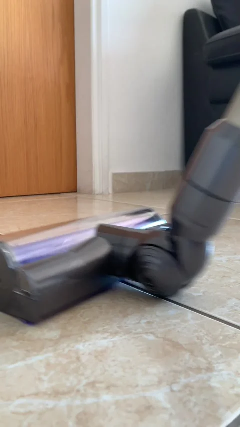 Close-up of a vacuum cleaner brush while cleaning. A woman or a man vacuums tile Stock Footage 220854814