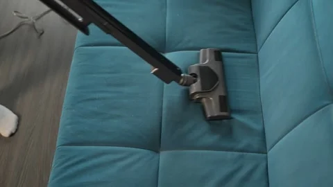 Close-up of a vacuum cleaner removing dirt from a blue sofa. Home care and Видео 306689508