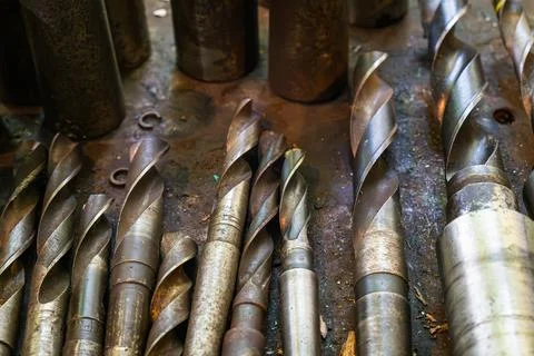 Close-up of various metal drill bits arranged on a workbench in a metalworking Stock Photos