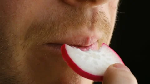 Close-up vegan man biting into radish, enjoying crunchy texture and refreshing Stock Footage 312847575