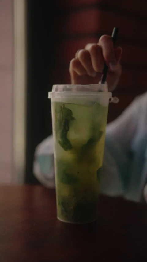 Close-up vertical cropped shot of relaxed person stirring delicious iced mojito 库存影片 342809319