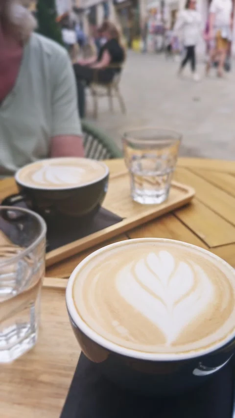 Close-up vertical of frothy cappuccino with latte art on an outdoor café table Stock Footage 341112737