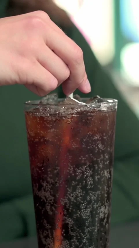 A close-up vertical shot of a hand stirring a fizzy iced soda in a glass with a Stock Footage 287318083