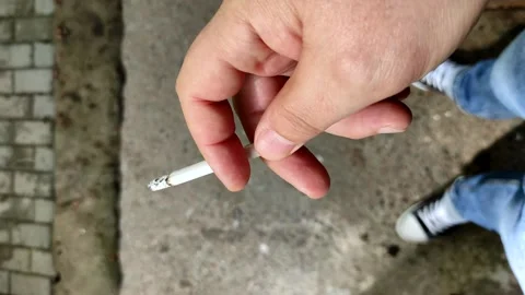 Close-up vertical video of a man's hand holding a smoking cigarette. Stock Footage 154333776