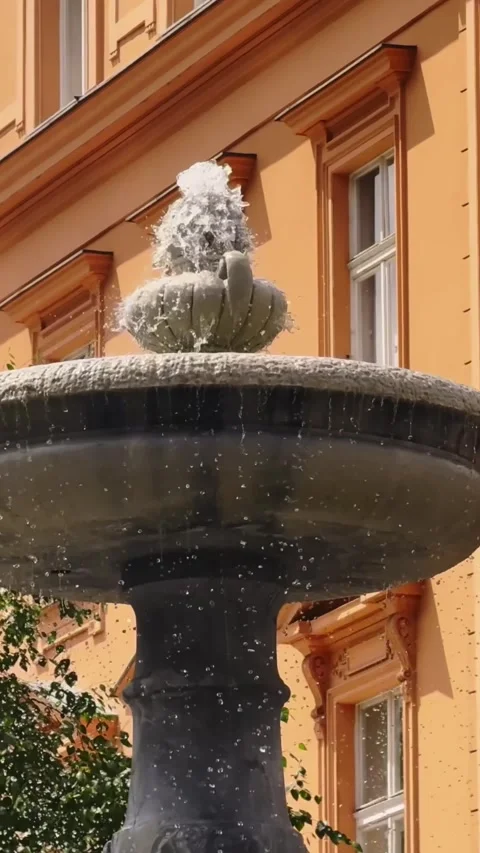 Close vertical view of a stone fountain spraying water beside a warm ochre Vídeo Stock 342488603