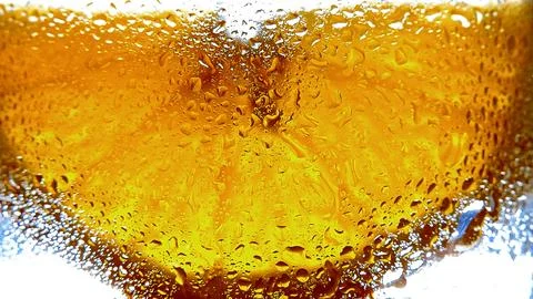 Close-up of vibrant orange slice behind glass with water droplets on surface. Stock Photos
