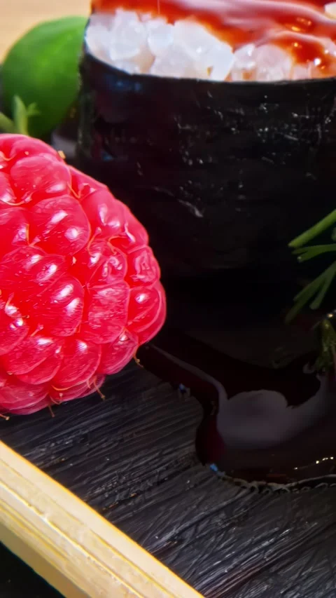 Close-Up of Vibrant Raspberry and Sushi Roll on Charred Wooden Surface Stock Footage 336333734