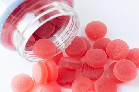 A close-up of vibrant red gummies placed next to a white container, highlight Foto stock